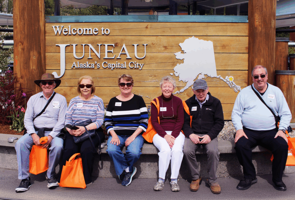 A group of people on tour with Juneau Food Tours sitting in front of the Welcome to Juneau sign.