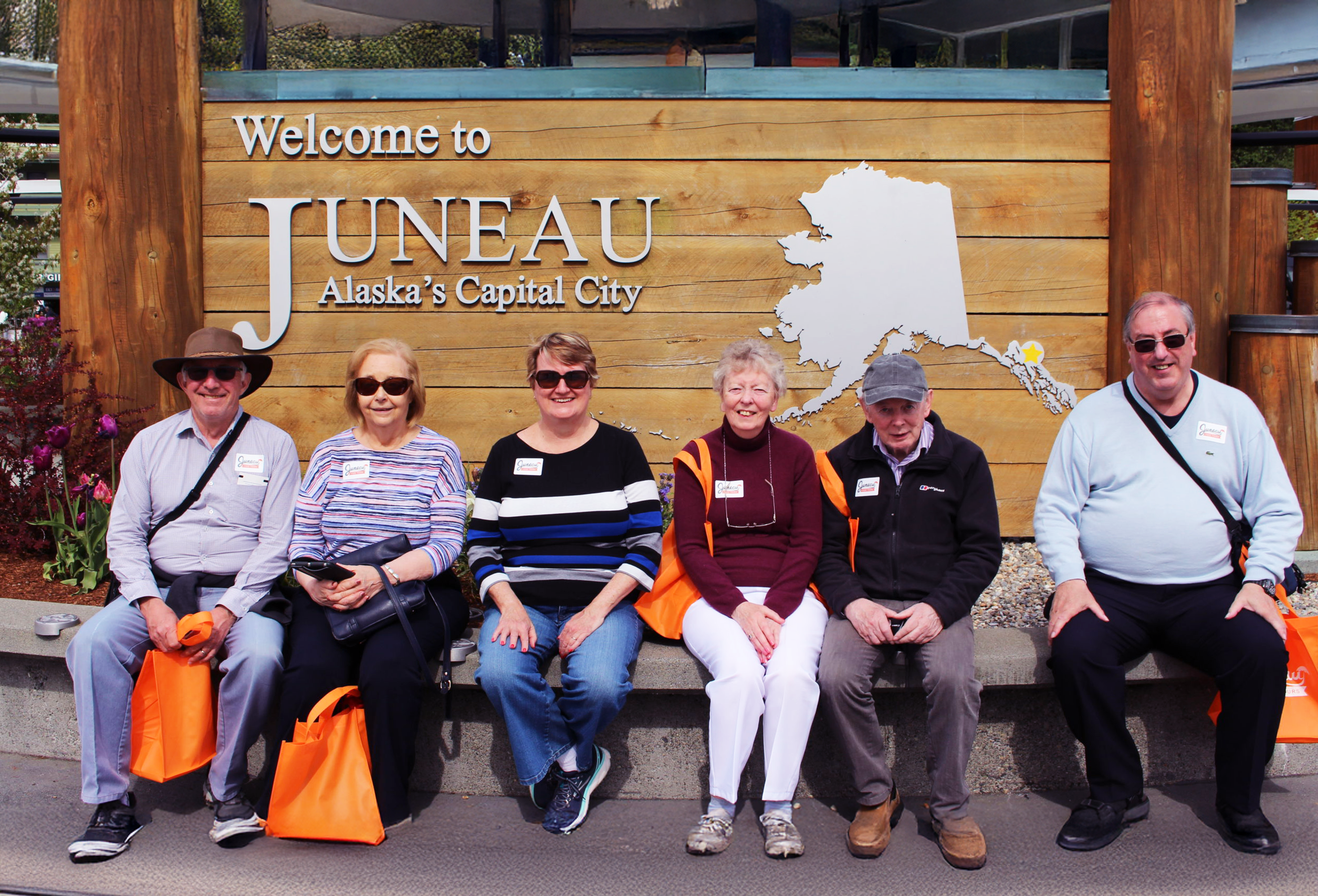 A group of people on tour with Juneau Food Tours sitting in front of the Welcome to Juneau sign.